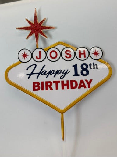 A novelty 18th birthday cake topper designed like a retro Las Vegas sign, featuring the name 'JOSH' in white circles with red stars, 'Happy 18th BIRTHDAY' in black and red script, and a red starburst topper on a white sign with a gold border.